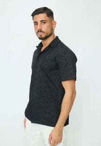 Chemise noire à manches courtes avec un motif géométrique texturé, col à boutons, coupe décontractée, fabriquée en tissu léger.