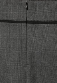 Karierte Stoffhosen in Schwarz und Grau, mit einem Reißverschluss, glatter Textur und dezenten Musterelementen.
