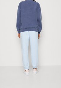 Mörkblå sweatshirt i oversize-passform med ribbade muddar. Ljusblå sweatpants med avsmalnande ben och elastiska muddar. Vita sneakers med mjuka detaljer.