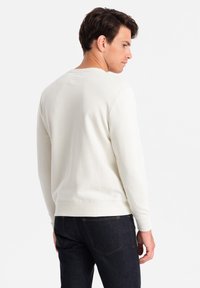 Světlý béžový svetr s kulatým výstřihem, žebrovanými manžetami a lemem, s hladkou texturou a minimalistickým designem. Nosit s tmavými džíny.