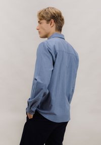 Lys blå langermet skjorte med myk tekstur, mansjetter med knapper, og en klassisk krage. Har rett bakre kant og subtile stingdetaljer.