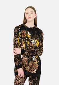 Hoodie noir à coupe surdimensionnée, avec un motif animalier de léopards dans des tons de marron et de jaune, tissu texturé avec des poignets et un ourlet côtelés.