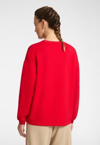 Felpa rossa con un fitting rilassato, spalle scese e polsini a costine; tessuto testurizzato; abbinata a pantaloni beige chiaro.