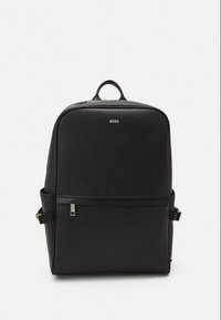 Zaino rettangolare nero con manico superiore, fibbie laterali, tasca frontale con zip e logo "BOSS" centrato vicino alla parte superiore.