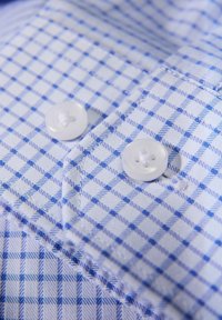 Camicia abbottonata con motivo a quadretti blu e bianchi, bottoni di plastica bianchi e tessuto dalla texture liscia.
