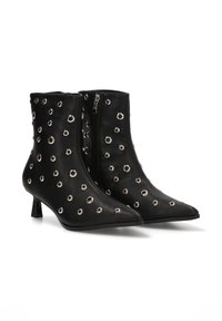 Botines negros de cuero liso, con adornos de ojales plateados, punta afilada y un tacón corto y ancho con cremallera lateral.