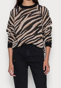 Maglione lavorato a maglia con motivo a strisce zebrate in nero, beige e marrone, con collo a giro e polsini a costine; indossato con jeans neri.