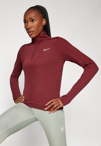 Burgundi hosszú ujjú sportfelső magas gallérral és negyed cipzárral. A mellkasán fényvisszaverő Nike logó található.