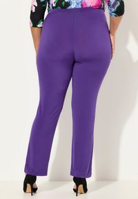 Fialové legíny s přiléhavým střihem, hladkým povrchem a rovnými nohavicemi. Kalhoty jsou doplněny černými lodičkami na podpatku.