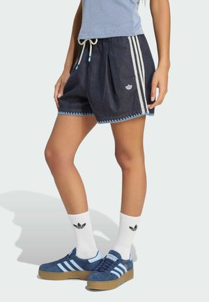 Ben iført marineblå Adidas-shorts med hvide striber, hvide Adidas mellemlange sokker og marineblå Adidas sneakers med gummisåler.
