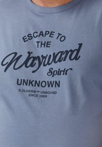 Blaues Baumwoll-T-Shirt mit schwarzem Drucktext: "ESCAPE TO THE Wayward Spirit UNKNOWN" und "S.OLIVER® UNBOUND SINCE 1969."