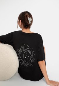Zwarte oversized t-shirt met een witte maan en ster grafiek met stralende lijnen op de achterkant; zachte stof met een ontspannen pasvorm.