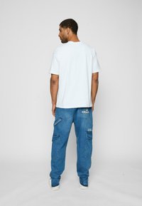 Lyseblå, kortærmet t-shirt parret med løstsiddende, blå denim cargo bukser med flere lommer og broderede detaljer.