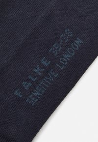 Chaussette en tricot bleu marine avec une texture douce. Présente un texte imprimé "FALKE SENSITIVE LONDON" en bleu plus clair près du haut.