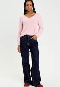 Vaaleanpunainen, pörröinen v-kaula-aukkoinen neule, yhdistettynä korkeavyötäröisiin, leveälahkeisiin tummansinisiin farkkuihin. Huomionarvoisia yksityiskohtia ovat taskut ja kontrastivindaukset.