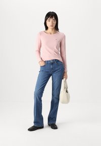 Ljusrosa långärmad ribbad topp, blå raka jeans med hög midja, svarta skor och en beige axelväska.