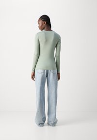 Lys grønn langermet topp med en tettsittende design, kombinert med løse lyseblå jeans. Enkel halslinje og jevn tekstur.