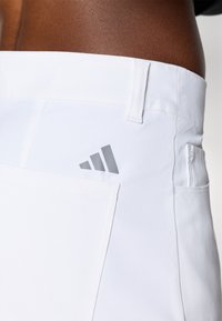 Bijele sportske kratke hlače glatke teksture, sa stražnjim džepom i sivim Adidas logotipom sa lijeve strane.