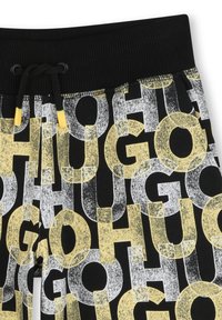 Shorts noirs avec une taille côtelée et un cordon de serrage. Présente un motif audacieux, répétitif de grandes lettres en gris, jaune et noir.