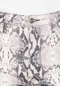 Bermudas de mezclilla blanca con un patrón de estampado de serpiente gris, herrajes plateados y un cierre de botón, con detalles de costura visibles a lo largo de las costuras.