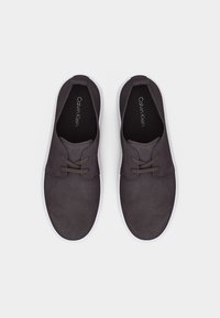 Ζευγάρι σκούρα γκρι σουέντ casual παπούτσια με κορδόνια και λευκές σόλες, σε λήψη από πάνω, με το λογότυπο Calvin Klein στο εσωτερικό.