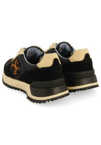 Chaussures de sport noires et beiges avec un accent en imprimé léopard ; elles présentent des matériaux en suède texturé et en cuir lisse, des semelles intérieures rembourrées et des semelles robustes.