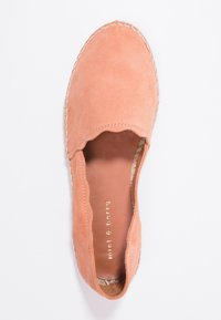 Chaussure slip-on en daim pêche avec bord festonné, semelle en jute et logo doré en relief sur la semelle intérieure. Texture lisse, design minimaliste.