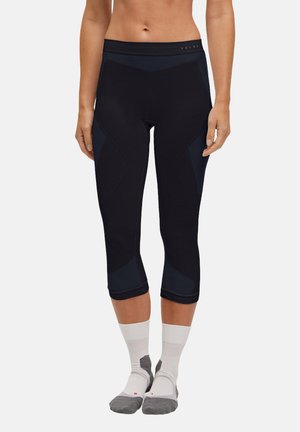 Pantalons capri de sport noirs avec un design ajusté, comportant des panneaux texturés et une taille haute, accompagnés de chaussettes de sport blanches et grises.