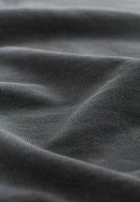 Tissu gris foncé à surface texturée, présentant des lignes et des plis subtils, suggérant un matériau lisse et extensible.