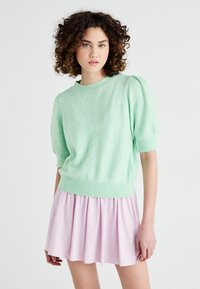 Mintgrön, kortärmad tröja i mjukt, fluffigt material med ribbat nederkant; kombinerad med en pastellrosa plisserad kjol. Enkel, avslappnad design.