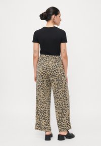 Zwarte korte mouwen t-shirt gecombineerd met een wijde leopardprint broek in beige en bruin, met een stretchy tailleband en subtiele textuur.