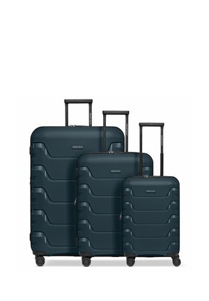 Trois valises rigides bleu foncé de différentes tailles avec des poignées télescopiques étendues et quatre roues chacune, disposées côte à côte.