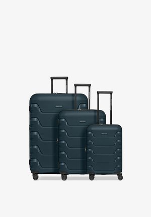 Trois valises rigides bleu foncé de différentes tailles avec des poignées télescopiques étendues et quatre roues chacune, disposées côte à côte.