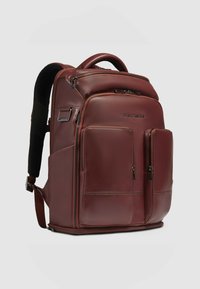 Brauner Lederrucksack mit mehreren Reißverschlusstaschen, ergonomischen Trägern und einem strukturierten Design. Merkmale sind ein Frontfach und Seitentaschen.