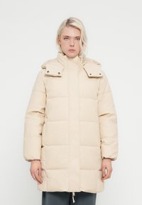 Casaco bege acolchoado com gola alta, botões de pressão e mangas compridas. Apresenta secções matelassadas e fecho de correr na parte inferior.