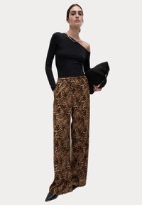 Svart enaxlad topp i kombination med bruna leopardmönstrade vida byxor. Modellen håller en strukturerad svart clutch och bär spetsiga svarta klackar.
