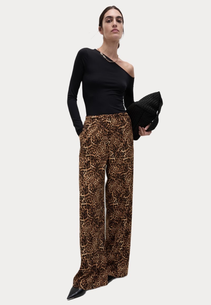 Svart enaxlad topp i kombination med bruna leopardmönstrade vida byxor. Modellen håller en strukturerad svart clutch och bär spetsiga svarta klackar.