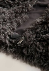 Sivá, nadýchaná fleece textília s detailom na zips. Textúra je mäkká a kučeravá, kontrastujúca s hladkým podšívkou.