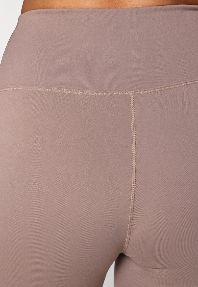 Lichtbruine leggings gemaakt van een gladde, rekbare stof, met een brede tailleband en een subtiele naaddetail aan de achterkant.