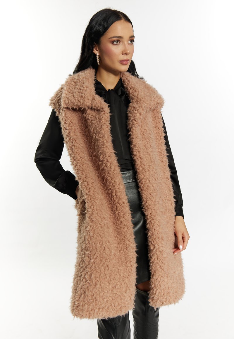 Faux-Fur-Weste in sanftem Blush-Pink, mit weitem Kragen und offener Vorderseite. Getragen über einer schwarzen Bluse und einem Lederrock.