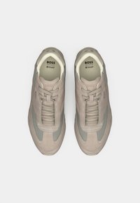 Ζευγάρι μπεζ και γκρι σουέντ αθλητικά παπούτσια BOSS με κορδόνια και εσωτερικά πέλματα Ortholite, σε θέα από ψηλά σε λευκό φόντο.