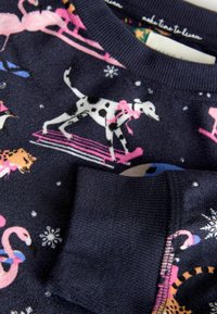 Mörkblå fleece-tröja med lekfullt djurmönster, som har rosa flamingos och en svartvit hund, ribbade ärmslut och mjuk textur.