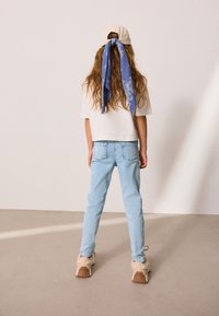 Vit kortärmad t-shirt, ljusblå jeans, beige sneakers med strukturerade sulor, samt en ljus färgad keps med en blå paisley-scarf knuten.