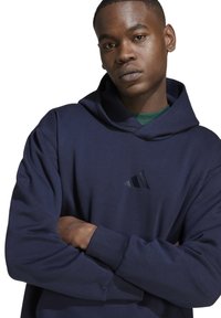 Felpa con cappuccio blu navy con logo ricamato e testurizzato sul petto. Presenta una vestibilità comoda e polsini a coste per il massimo comfort.
