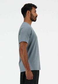 Maglietta azzurra chiara a maniche corte con una finitura testurizzata e dettagli di ventilazione laterale, abbinata a pantaloni corti scuri a motivi, vista di lato.