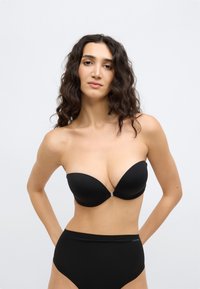 Μαύρο σουτιέν χωρίς τιράντες με απαλή, ματ υφή και βαθύ ντεκολτέ, με ασημένιο κούμπωμα στο κέντρο. Μαύρο σλιπ ψηλόμεσο.