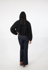 Sort cropped sweatshirt med brede ærmer og ribbet kant, kombineret med udvidede mørke denimjeans og brune sko med chunky hæl.