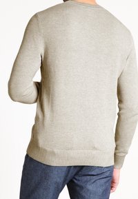 Pull gris clair en tricot avec un motif texturé, col rond, poignets et ourlet côtelés. Porté avec un pantalon bleu foncé.