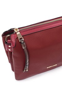 Borsa a tracolla rossa in pelle con finitura testurizzata, zip dorata e un accento decorativo con motivo a serpente sulla tracolla.
