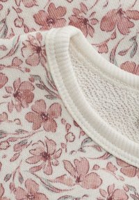 Bloemmotief stof in zachtroze en wit. Inclusief een geribbelde ronde hals met een gestructureerde binnenvoering voor comfort.